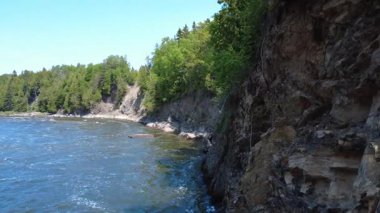 Somon Nehri üzerinde insansız hava aracı uçuşu, bahar selinde Mitis Nehri ve Kanada 'nın Quebec kentinde mavi bir gökyüzü altında yeşil ormanla çevrili kayalık uçurumlar..