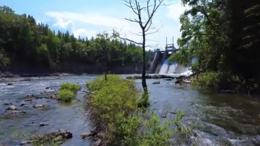Drone videosu bitki örtüsünün üzerinden nehrin üzerinden geçerek geçidi antik bir kale gibi tamamen kapatan elektrik barajına doğru uçuyor. Mitis-2 Üretim İstasyonu, Price, Quebec, Kanada.