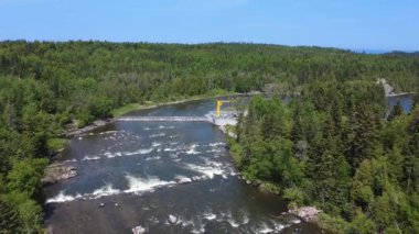 Bulutsuz mavi gökyüzünün altındaki ormanın içinden geçen ünlü ve dolambaçlı Mitis Nehri 'ne kurulmuş bir somon tuzağının hava manzarası ve kalıcı bir somon tuzağı. Quebec, Kanada.