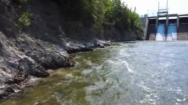 Mitis Nehri 'nin ve kayalık uçurum kıyılarının üzerindeki bir manzara, bir hidroelektrik barajının beton duvarının üzerinden akan suyu boşaltan şelalelere kadar ormanla kaplı. Mitis-2, Price (Quebec), Kanada.