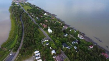 Sakin sularla ve yemyeşil alanlarla çevrili ve doğa ile geleneksel liman mimarisi arasındaki uyumu vurgulayan pitoresk bir yarımada boyunca uzanan bir kıyı köyünün panoramik hava manzarası.
