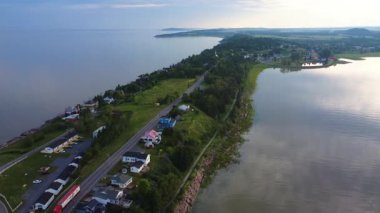 Sakin sular boyunca yemyeşil yeşeren sakin bir kıyı manzarasının panoramik hava manzarası, küçük evler ve ağaçlar pitoresk bir ortam oluşturuyor. Riviere-du-Loup, Quebec, Kanada, 2025.