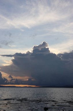 Banliyölerde sakin bir sahil manzarası, sakin deniz suyu, bulutlar, dağlar, ağaçlar ve öğleden sonra güzel gökyüzü.