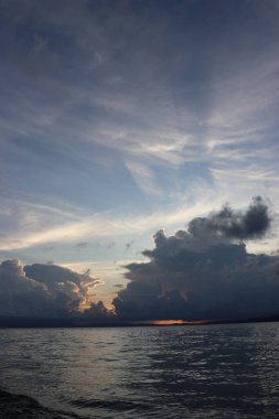 Banliyölerde sakin bir sahil manzarası, sakin deniz suyu, bulutlar, dağlar, ağaçlar ve öğleden sonra güzel gökyüzü.