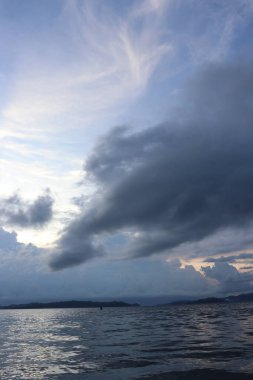 Banliyölerde sakin bir sahil manzarası, sakin deniz suyu, bulutlar, dağlar, ağaçlar ve öğleden sonra güzel gökyüzü.