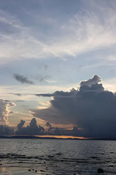 Banliyölerde sakin bir sahil manzarası, sakin deniz suyu, bulutlar, dağlar, ağaçlar ve öğleden sonra güzel gökyüzü.
