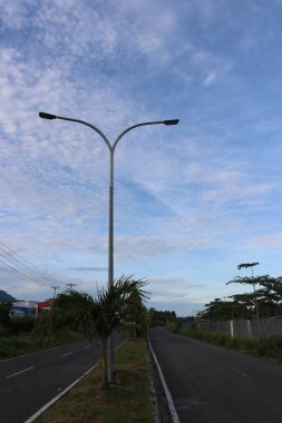 Yol kenarındaki yeşil ağaçların ve yaprakların gölgeli bulutların ve mavi gökyüzünün görüntüsü.