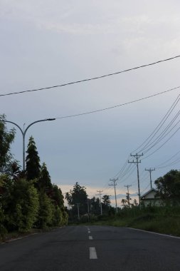 Yol kenarındaki yeşil ağaçların ve yaprakların gölgeli bulutların ve mavi gökyüzünün görüntüsü.
