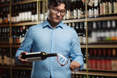 Dikkatle konsantre olan, mavi gömlekli profesyonel Asyalı şarap garsonunun şişeden saplı cama kırmızı şarap dökerek geniş bir rafla doldurulduğu görüldü.