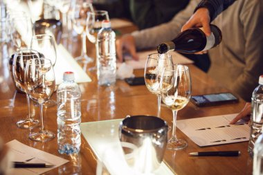 Şarap tatma etkinliği ya da akşam yemeği sırasında masaya bir bardak beyaz şarap koyarken gösteriliyor.. 