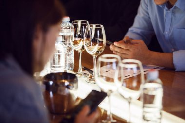 Several filled wine glasses are meticulously aligned on a table during sitting sommeliers engage in discussion about the characteristics or origins of the wines.  clipart