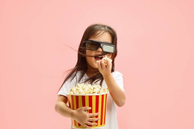 Üç boyutlu gözlüklü tatlı Koreli bir kızın, kameraya bakarak patlamış mısır yediği, saçlarının farklı yönlere uçtuğu, beyaz bir tişört giydiği,