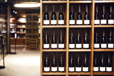 Şarap şişeleri bir dükkanda ahşap raflarda dizilmiş, şaraphanenin içi köpüklü şarapla dolu..