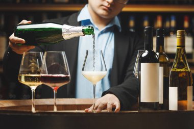 Kapalı mekanda yüzü olmayan şarap garsonunun fotoğrafı mahzende şampanyayı şişeden bardağa döküyor..