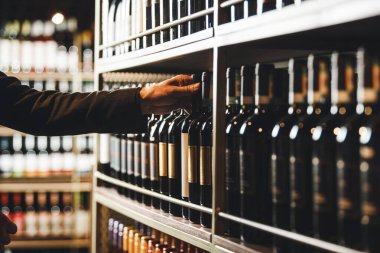 Sommeliers 'ın eli titizlikle organize edilmiş bir şarap rafına uzanır ve ziyaretçi isteğini karşılamak için mükemmel bir şişe seçer. Raflarda bir sürü kaliteli şarap şişesi var.