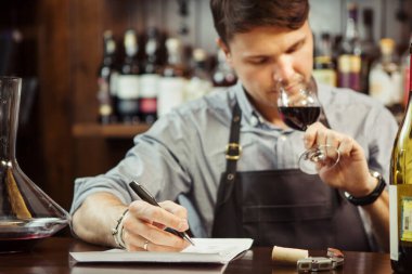 Erkek sommelier kırmızı şarap tatma ve sayaç bar, notlar. Şişe şarap. Profesyonel uzman Alkollü Içki, degüstasyon işlem kalitesini takdir eder.