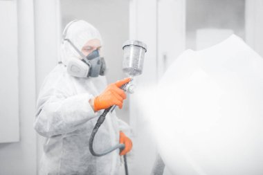 Profesyonel erkek araba boyacısı garajda boya yapıyor. İşçi aracı sprey tabancayla boyuyor. Kazadan sonra otomobilin onarımı.