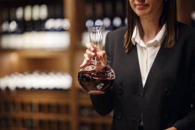 Kadın şarap garsonunun mahzende bir sürü içkiyle kırmızı şarap içerken yakın plan çekimleri. Şarap yapma mesleği.