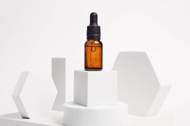 Pipetli kahverengi cam serum kabı, izole edilmiş arka planda geometrik şekillerle çevrili beyaz bir yavrunun üzerinde. Mesaj için yer. Masaj, spa, aromaterapi, kozmetoloji kataloğu, afiş