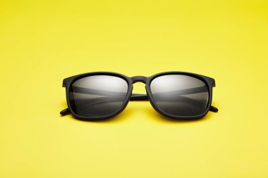 Siyah güneş gözlüğü klasik katlanmış model. Güneş gözlükleri, güneş gözlükleri, güneşli sarı arka planda izole edilmiş güneşlikler. Uzayı kopyala Yaz kataloğu için şablon, reklamlar. Güneş ışığına karşı suç ortağı koruması.
