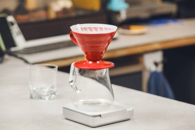 Kırmızı Hario V60 kahve hunisi cam sürahinin üzerine tünemiş, dijital ölçekte duruyor, özel kahve demleme işlemine hazır.. 