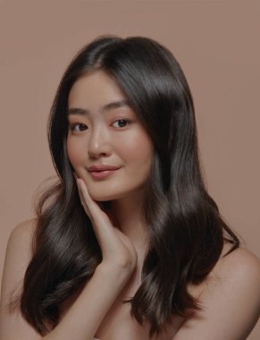 Güzel esmer Asyalı bir kadının stüdyo portresi. Temiz ve sağlıklı bir cilde sahip. Yüzüne bej arka planda dokunuyor.. 