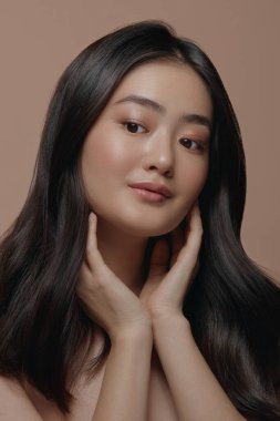 Güzel Asyalı kadın temiz ve sağlıklı cildine dokunuyor, bej arka planda dikey portreyi kapatıyor. Cilt bakımı, kozmetoloji ve estetik cerrahi konsepti. Asyalı bir kadının güzel bir yüzü var.