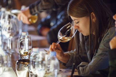 Bir grup birey masanın etrafında oturuyor, sohbet ediyor ve şaraptan zevk alıyorlar. Dişi şarap garsonu, bir degukasyon sırasında beyaz şarap tadıyor..