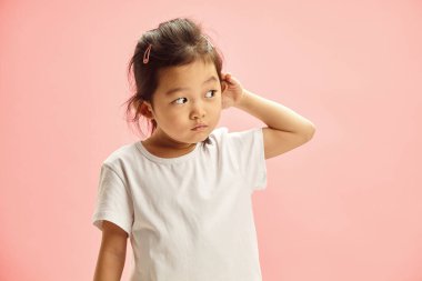 Studio portrait of curiosity five year old Asian ethnicity child girl overhearing someone elses conversation, what adults are talking about, whats going on behind the wall, intenly listen looking clipart