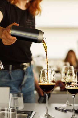 Unrecognizable woman pouring stout beer to participant during type tasting, close up. Blind beer tasting. Beer school, beer craft lecture. clipart