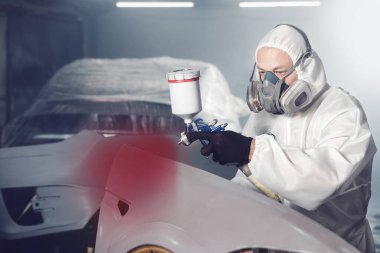 Araba boyacısı atölye garajında sprey tabanca kullanarak aracın bir kısmına kırmızı boya püskürtür. Boya odasında çalışan adam. Karmaşık onarım ve restorasyon otomobili sonrasında tam renk seçimi