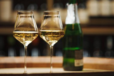 İki bardak köpüklü şarabı ahşap fıçının üzerinde yeşil cam şişe şampanyaya yakın tut..