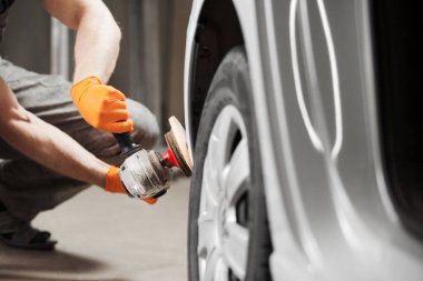 Araba temizleme serisi: oto tamirhanesinde beyaz araç cilalama. Erkek işçi otomobilin kaportasını tamir etti.