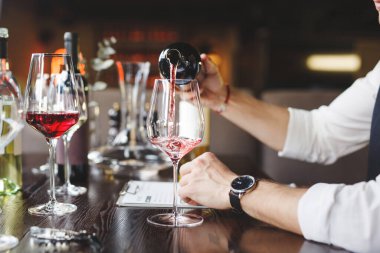 Meçhul şarap garsonu restorandaki masaya kırmızı şarap koyuyor. Kutlamaya hazırlanıyorum. Bardakları dolduran erkek elleri. Garson içki servisiyle uğraşıyor. Yakın plan. Yan görünüm.