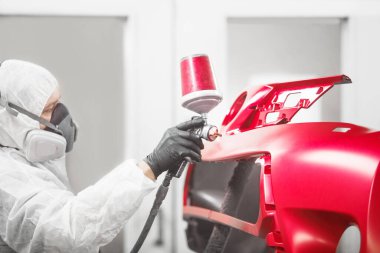Auto makinist işçisi resim araba tampon boya tabancası ile bir boya odasında onarım çalışmaları sırasında. Aracın tamir restorasyonu için servis.