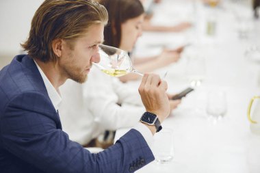 Beyaz şarap tatmak için klasik süitte giyinmiş beyaz şarap içen beyaz ırktan profesyonel bir şarap garsonu, uzmanlık eğitimi sırasında lezzet, renk ve asit seviyelerini analiz eder.