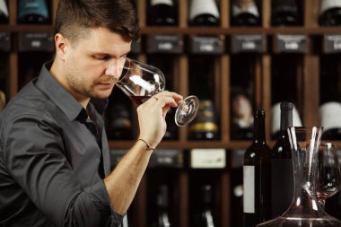 Sommelier şarap mahzende, adam holding cam döktü kırmızı alkollü sıvı İçecek kalitesi, mantarlar ve etiket sahip şişeler içeren tablo tanımlamak için parfüm koklama ile degüstasyon süreci