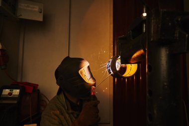 Koruyucu maske takan işçilerin portresi metalleri kaynaklıyor. Fabrikadaki kaynakçı..