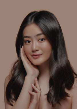 Güzel esmer Asyalı bir kadının stüdyo portresi. Temiz ve sağlıklı bir cilde sahip. Yüzüne bej arka planda dokunuyor.. 