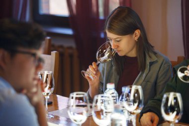 Kadın sommelier masada oturuyor, profesyonel gelişim eğitimi alıyor, kadehten şarap tadıyor, aroma ve lezzet notlarına odaklanıyor..