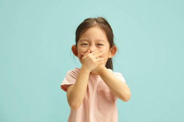 Neşeli Asyalı etnik kökenli, Eli Mouth 'un üstünde olan kız çocuğu, gerçeği söylemek istemiyor, kahkahalarını zor zapt ediyor, mavi izole edilmiş bir şeyin başında duran bir şey hakkında sessiz kalmaya çalışıyor.