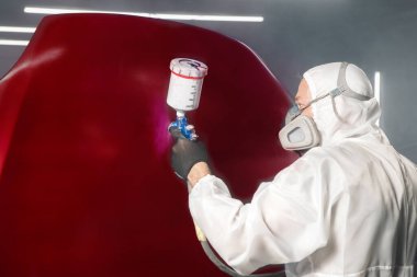 Araba tamircisinin elleri koruyucu iş kıyafetleriyle hava fırçasıyla boya odasındaki cesedi boyuyor. Adam sprey tabancayla çalışıyor. Vücut tamir arabaları.