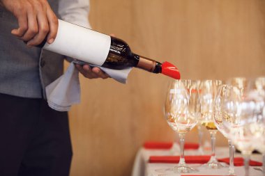 Close up faceless photo of bartender pouring white wine from untitled bottle to the glasses during blind tasting session. Training for sommelier and staff for alcoholic beverages. Exam for get clipart