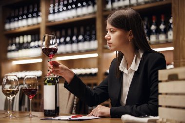 Young beautiful woman sommelier tasting red wine in the wine cellar, close up photo. Alcoholic beverages degustation. Winemaking school, wine waiter certification. Association of professional clipart