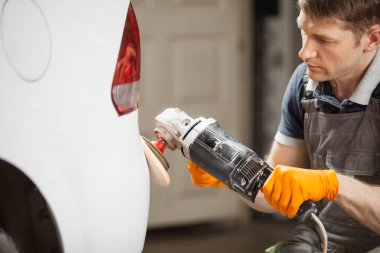 Beyaz arabanın cilalanması, cilalama makinesi ile çalışan işçiler kaportayı kurtarır. Otomobil tamiri. Resim yaptıktan sonra son tedavi.