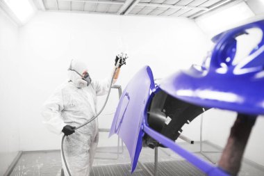 Araba boyacısı boya kabininde cila sıkar. Otomobil gövde onarımı.