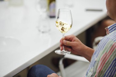 Close up photo of skilled sommelier tasting white wine during wine experts training on winemaking courses. Male hand swirling glass of wine, faceless shot. Professional man tasting white wine. clipart