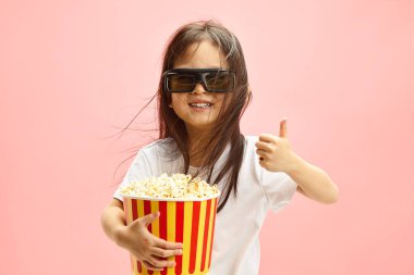 Büyük boy 3D gözlükleri ve klasik kırmızı ve sarı çizgili patlamış mısır kovasını tutarak film deneyimine kendini kaptırmış küçük Japon kızın stüdyo portresi.