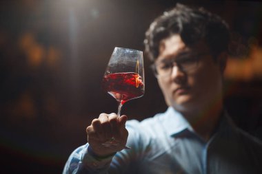 Profesyonel şarap garsonu berraklık, renk ve kırmızı şarabın berrak camdaki tutarlılığını değerlendirmeye odaklanırken, mahzenlerin çevre aydınlatması olay yerine yumuşak bir ışık sağlıyor..