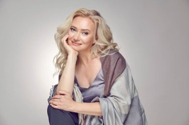 Çalıntı ekoseli bir elbise giymiş, gri izole bir arka planda, 50 yıllık lüks bir kadının stüdyo portresi. Mutlu gülümseyen olgun kadın sana bakıyor..